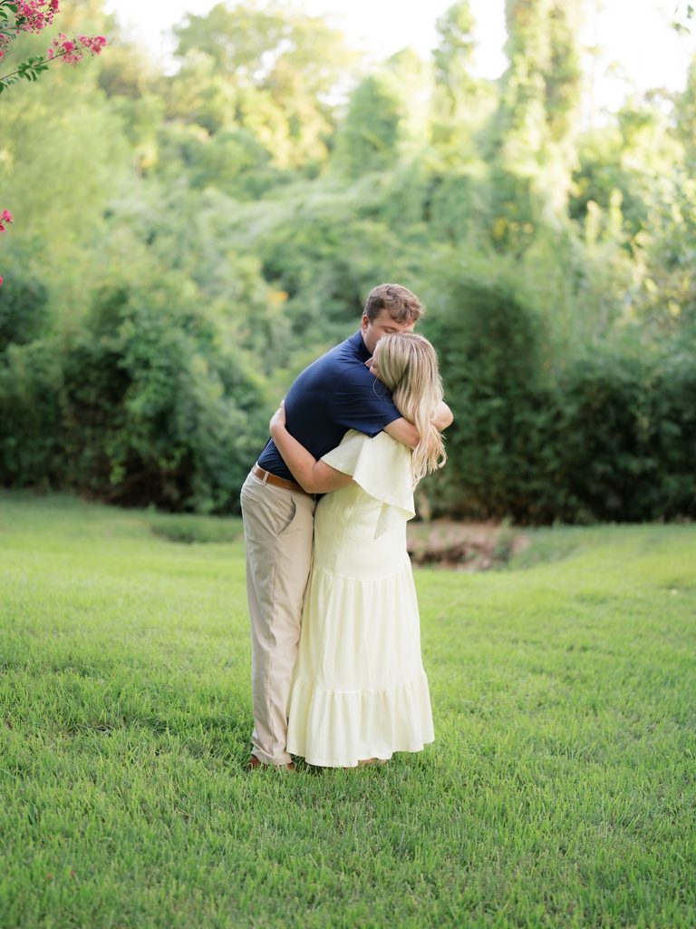 Groom-to-be kissing his fiancée on the head in a tender embrace on the grassy lawn after the proposal