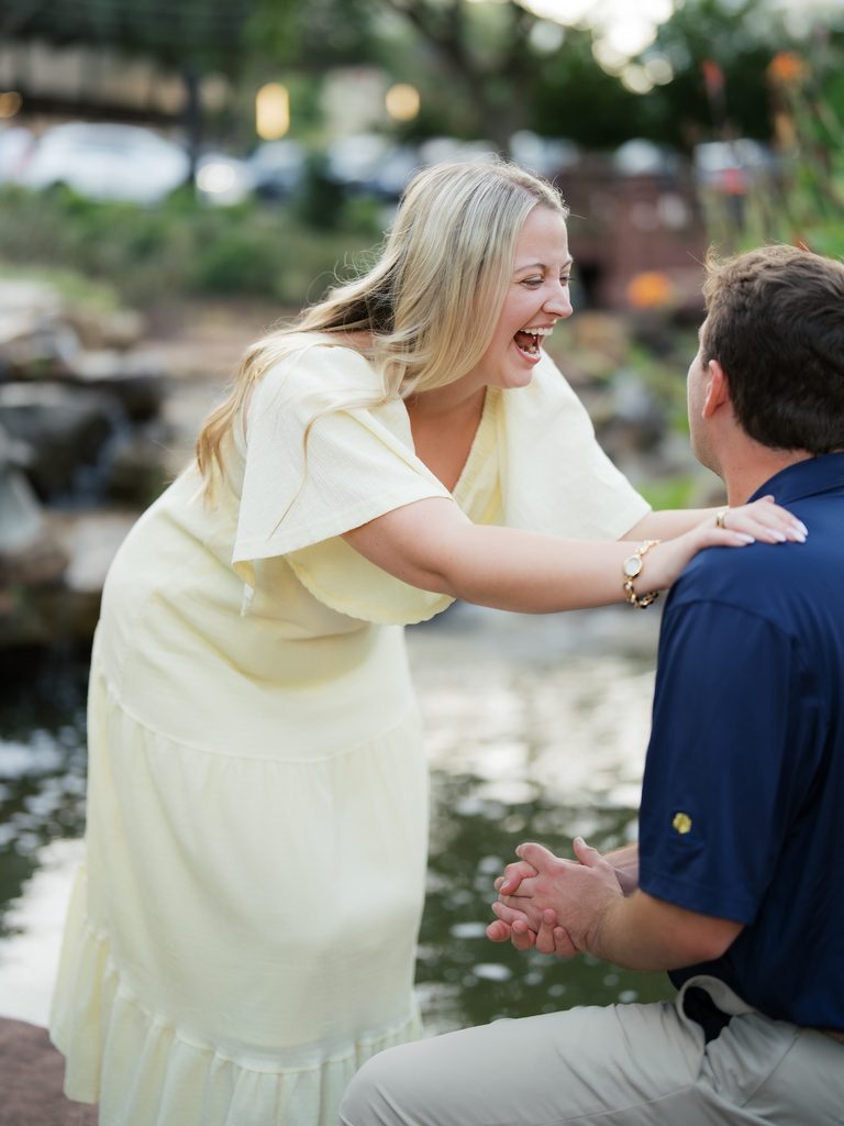 Excited bride-to-be laughing and leaning in with her hands on her fiancé's shoulders right after saying yes