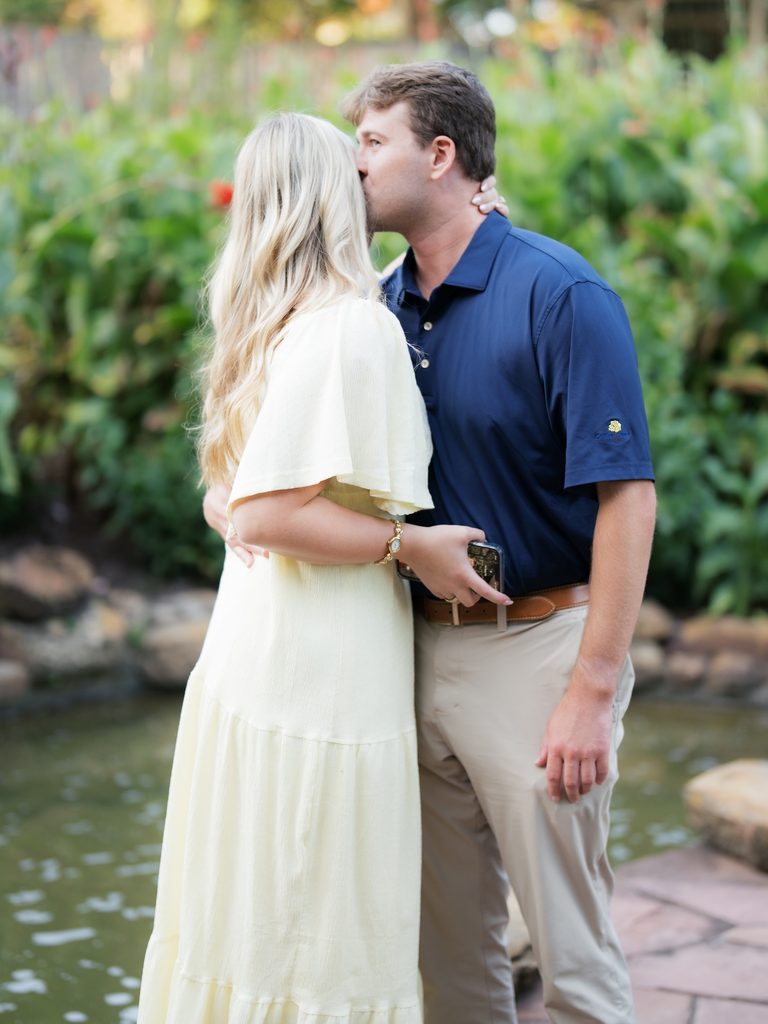 Soon to be groom kissing his fiancée on the forehead beside the pond, a quiet moment during their Houston proposal at Brenners on the Bayou