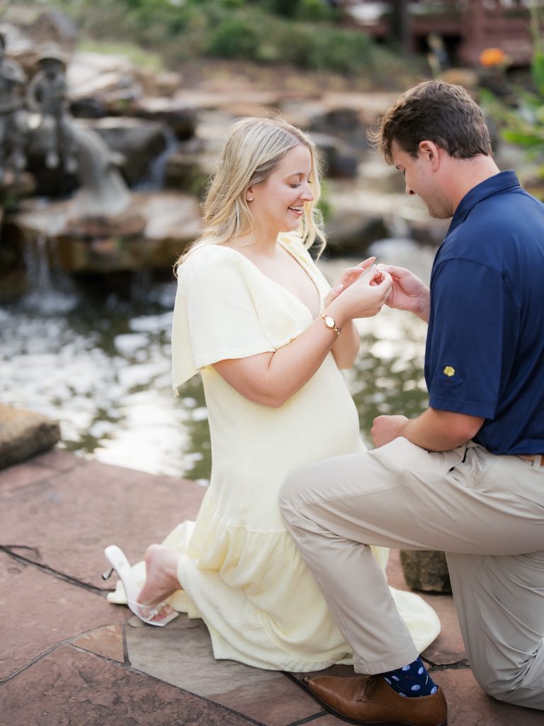 Groom sliding the engagement ring onto his fiancée's finger beside a garden stream at their Houston proposal