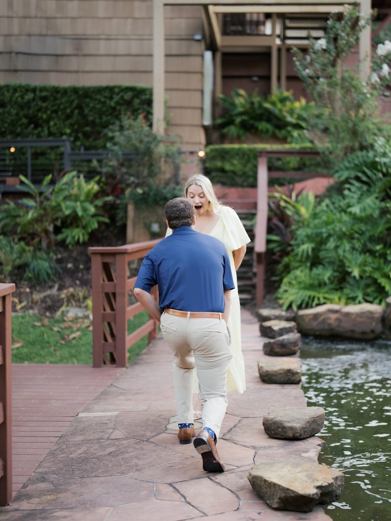 Surprised bride-to-be gasping as her boyfriend approaches on the stone path just before he proposes