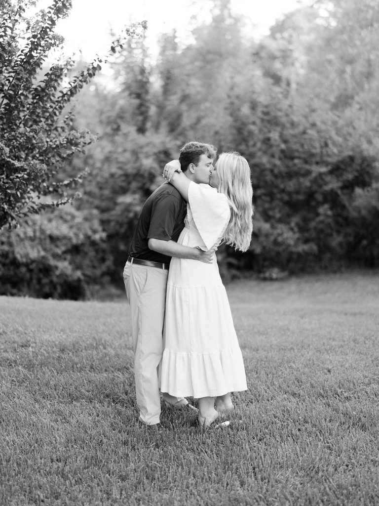 Timeless black and white photo of an engaged couple kissing in a grassy garden after the proposal