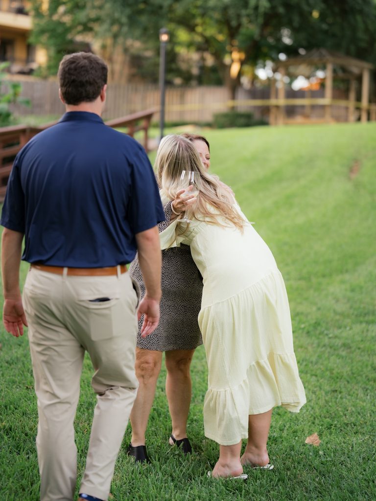 Groom-to-be walking toward loved ones as the bride-to-be hugs a guest with a glass of white wine at a Brenners on the Bayou proposal