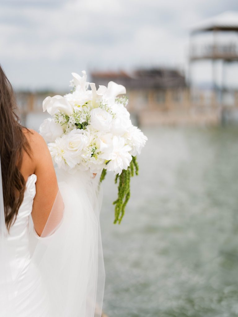 Bridal photos detail of a white and green bouquet held at the water’s edge, sheer veil in the foreground