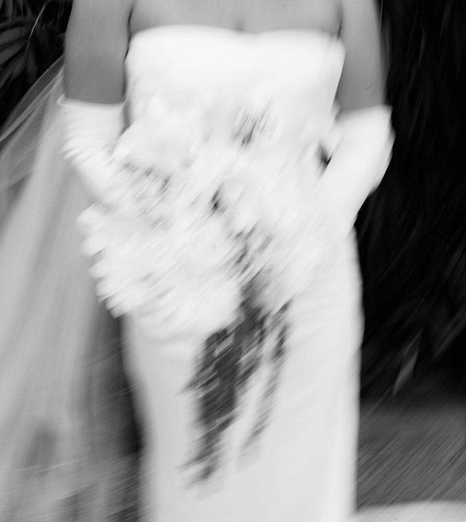 Black and white motion-blur photo of a bridal bouquet and satin gown in movement