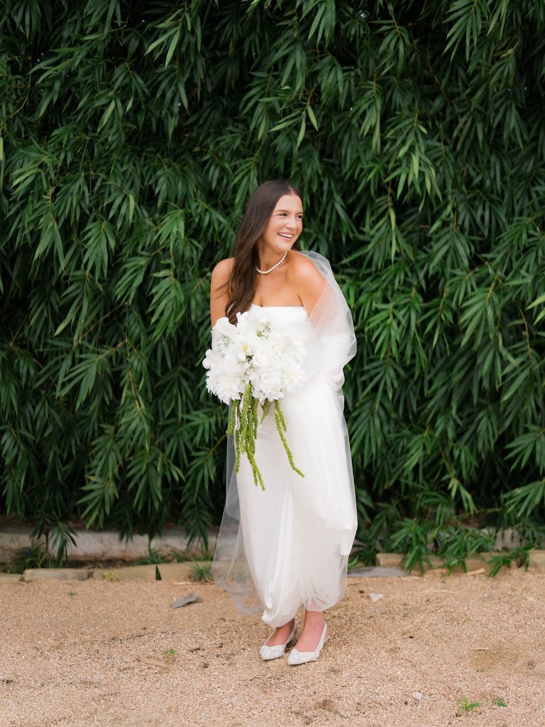 Bridal photos of a bride laughing in front of a bamboo wall, veil draped over her arms, wearing lace slingback flats